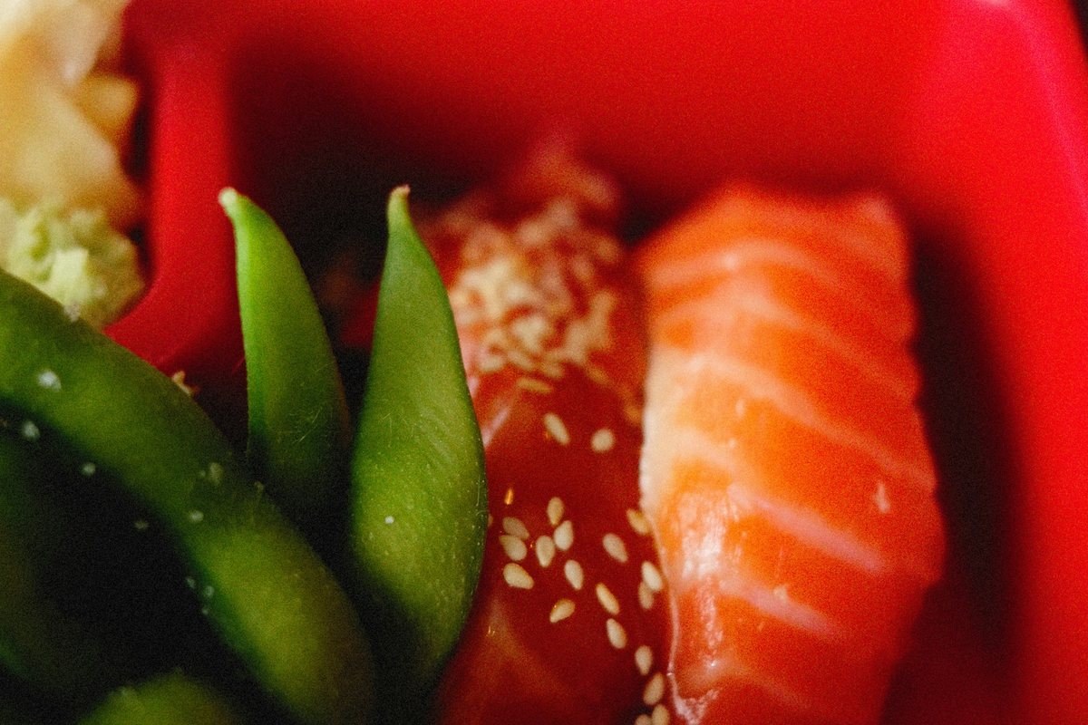 Close-up of a red bento box with sushi, salmon and edamame
