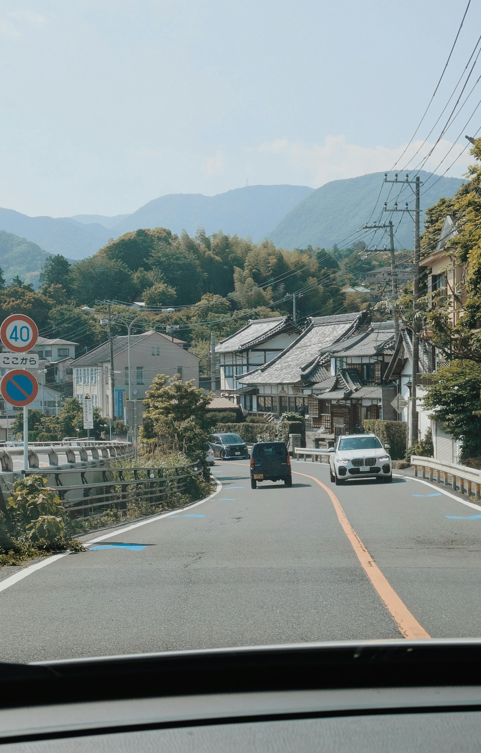 Cars driving down a narrow road through a Japanese hillside town