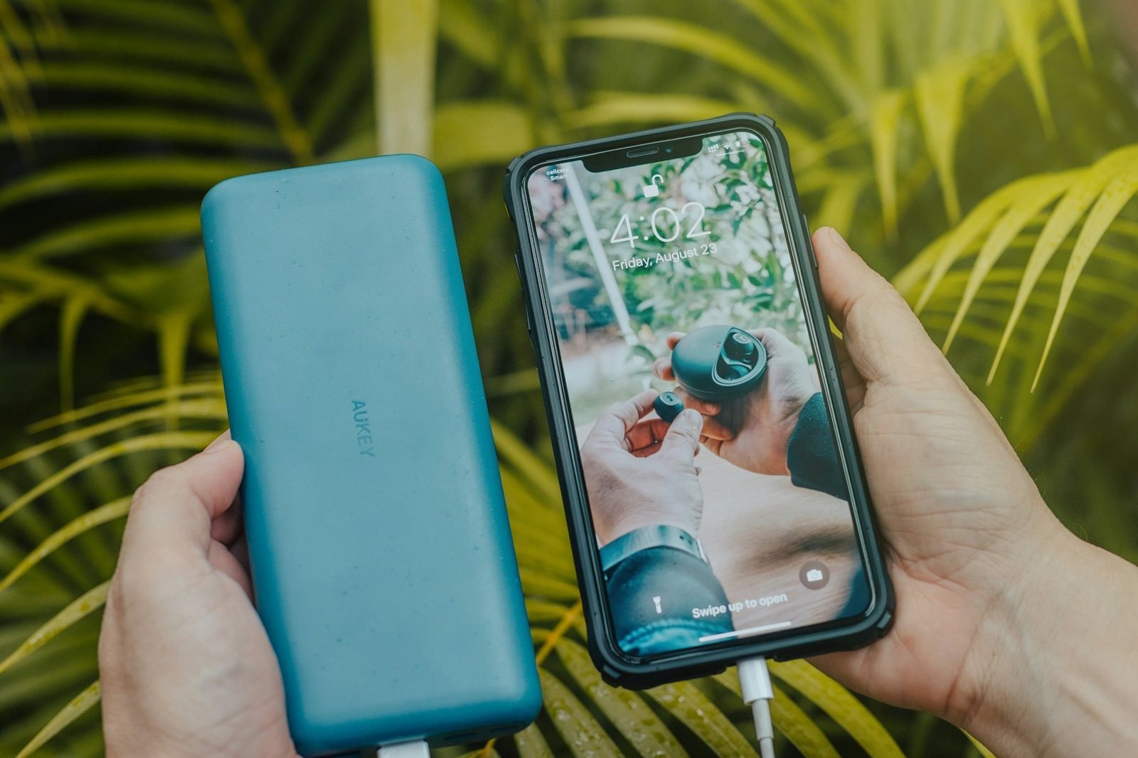 Hands holding a teal power bank and a smartphone that is charging