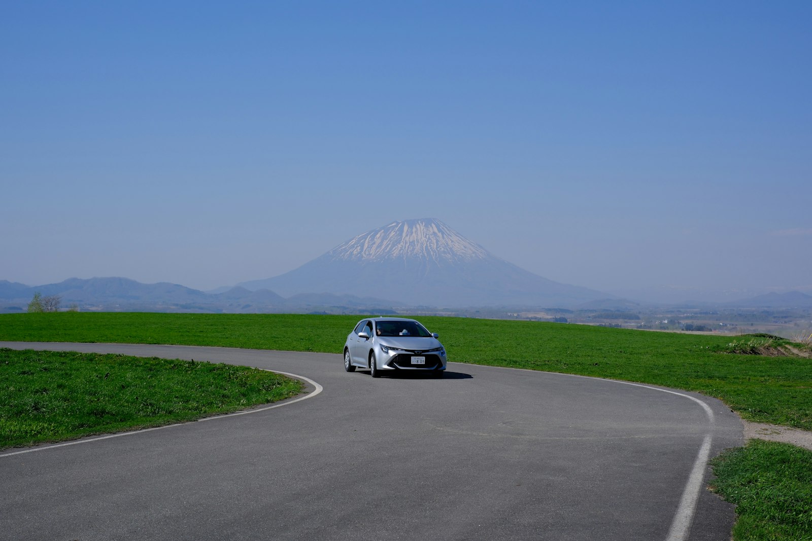 Car on an open road in Hokkaido with a mountain on the horizon
