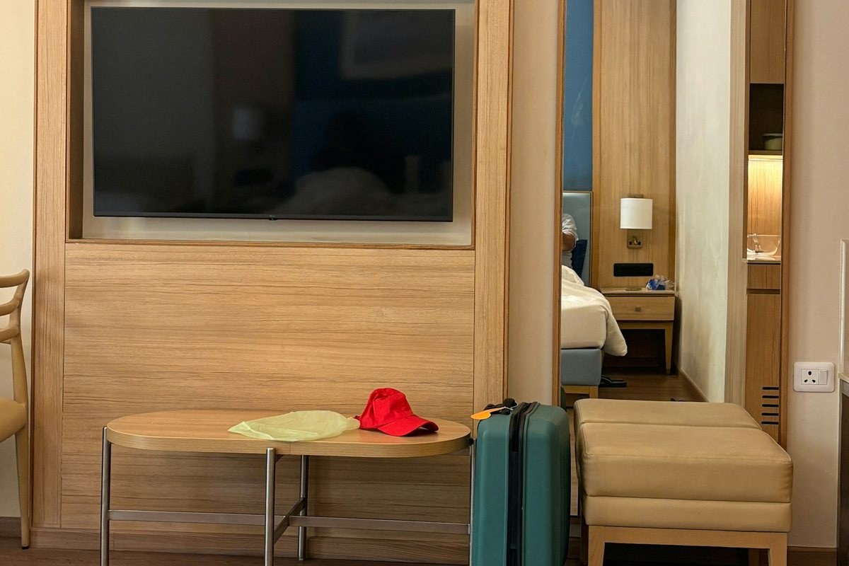 Hotel room with wooden furniture and a small suitcase, showing limited floor space