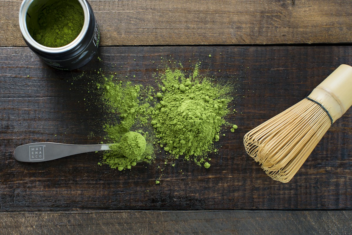 Matcha powder with a bamboo whisk and scoop on a wooden table