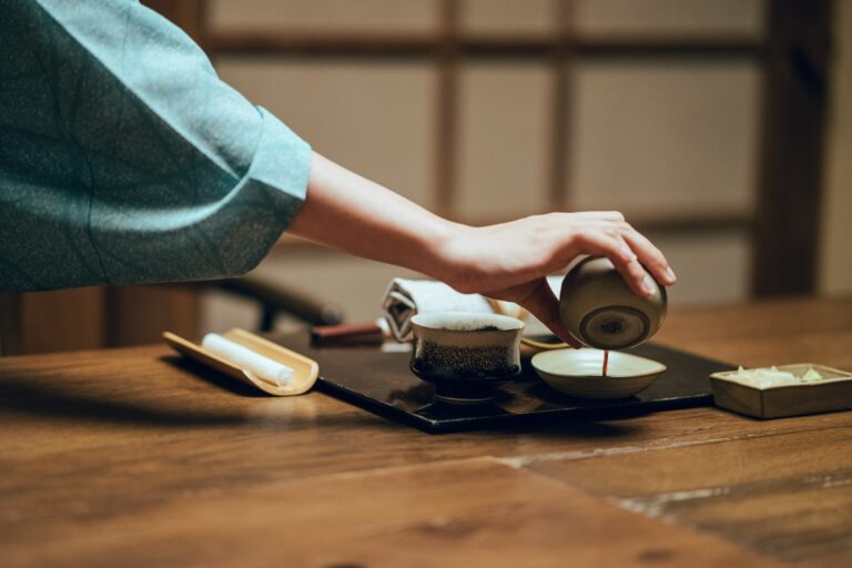 Person pouring Japanese tea at a low wooden table