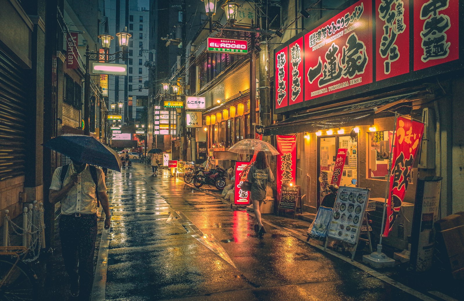 People with umbrellas walking down a rainy street lined with glowing shop signs in Japan