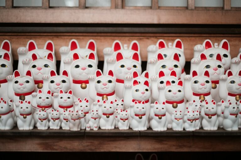Rows of white maneki-neko lucky cat figurines on a wooden shelf at a Japanese temple