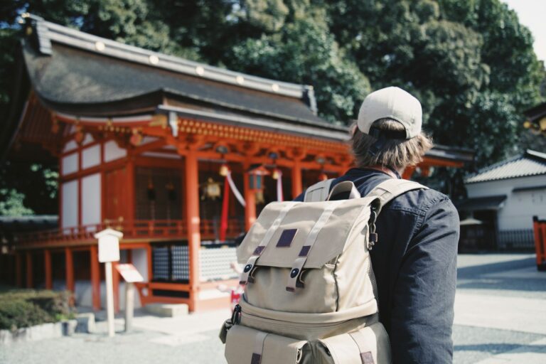 Traveler with a backpack walking past a red Japanese shrine building