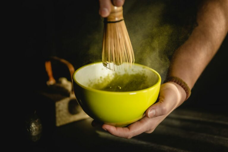 Hands whisking matcha with a bamboo whisk in a bowl