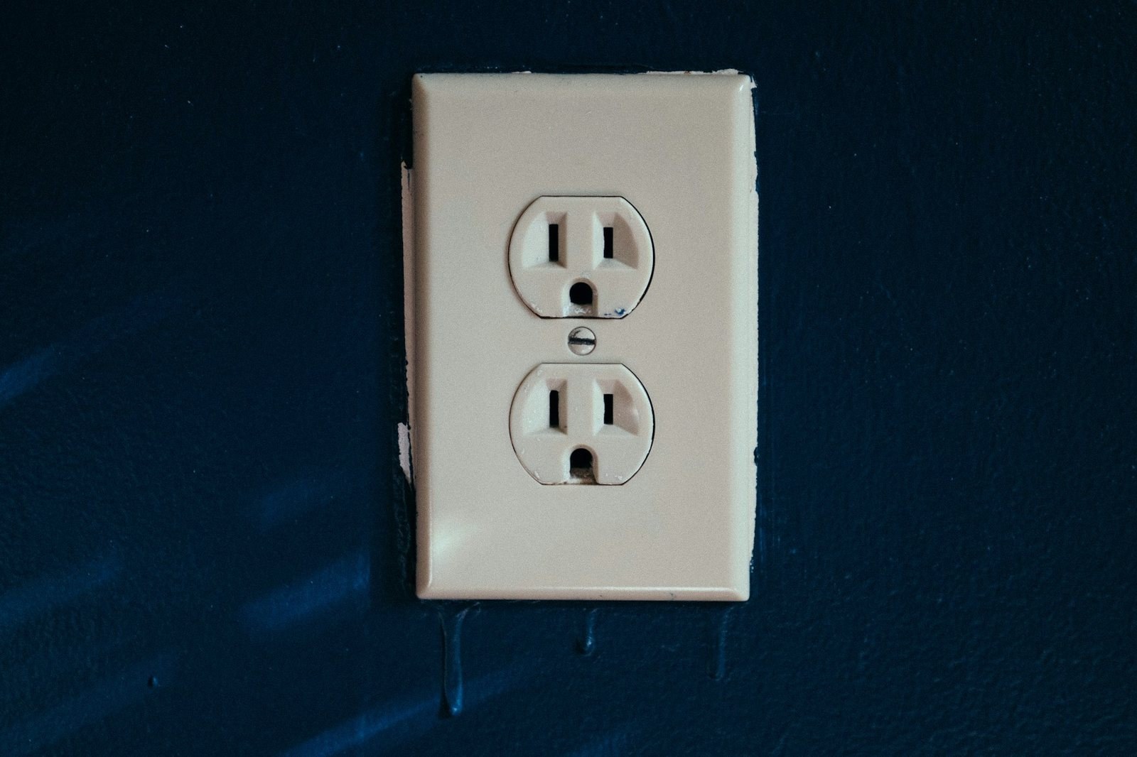 White electrical outlet with three-prong sockets on a navy blue wall