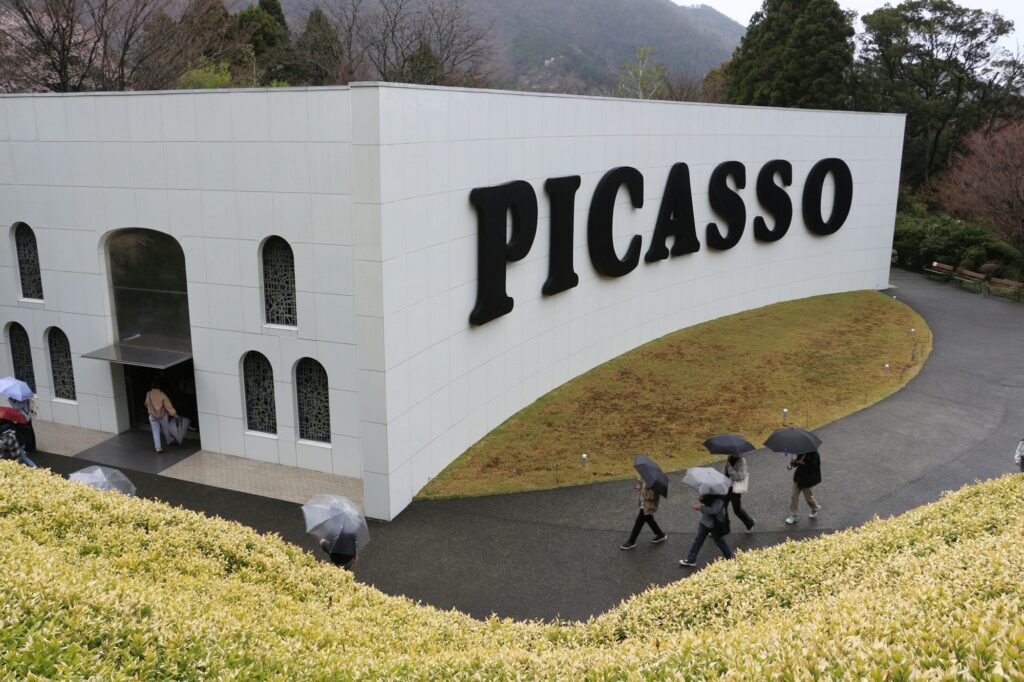 Visitors with umbrellas walking past the Picasso Pavilion at the Hakone Open-Air Museum