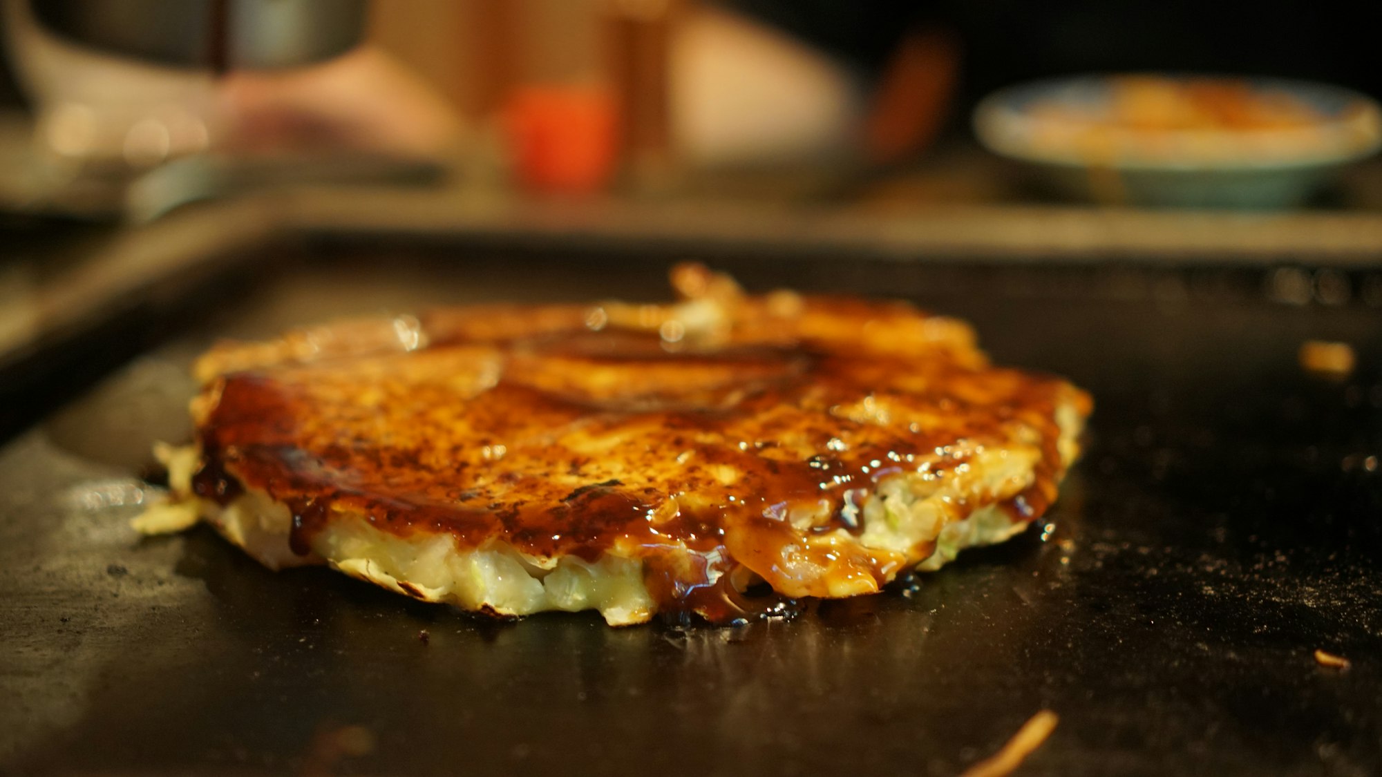 A layered okonomiyaki cooking on a hot iron griddle