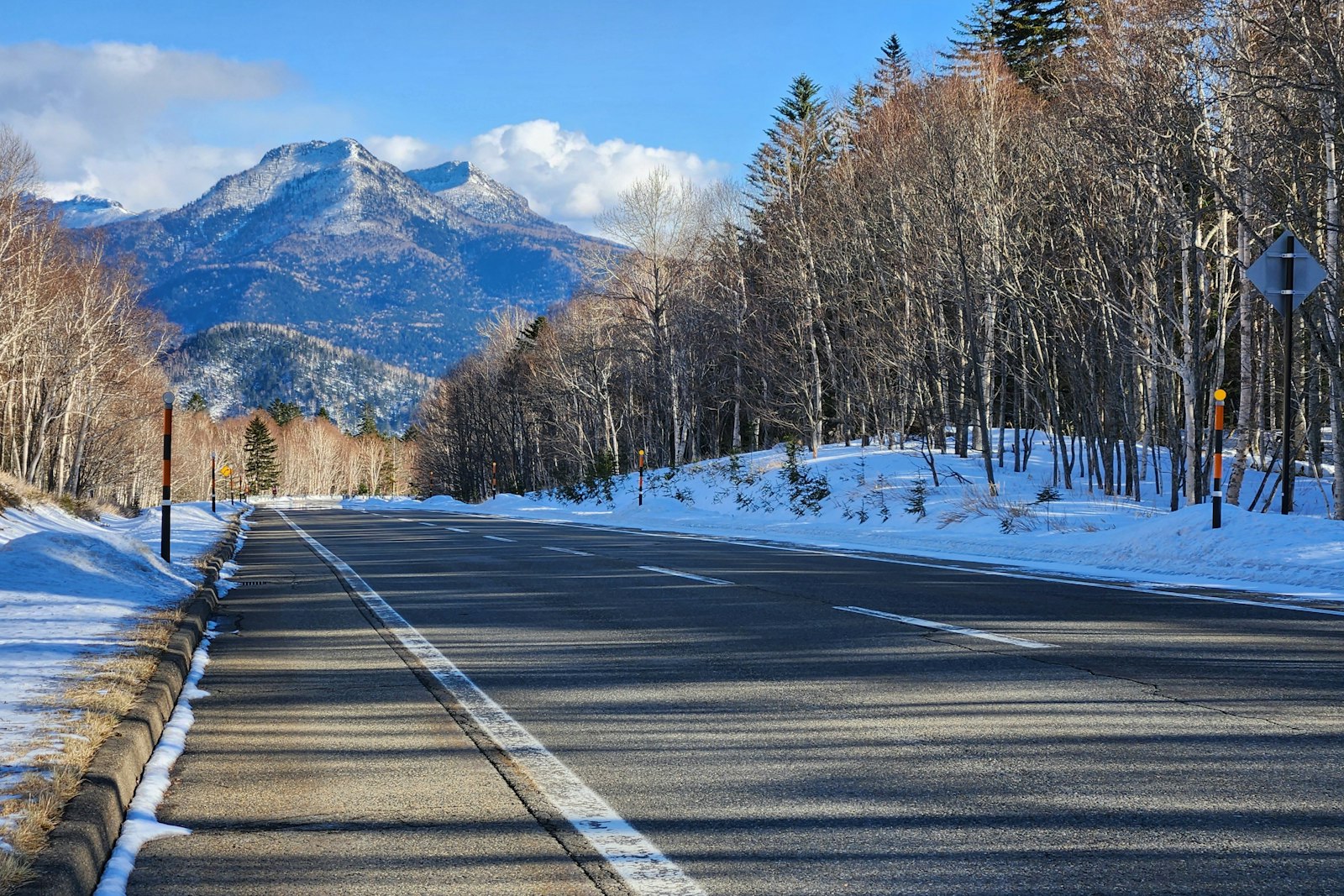 Cleared two-lane road with snowbanks and mountains in Kamishihoro, Hokkaido