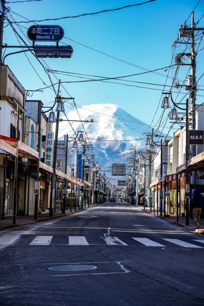 Snow-capped Mount Fuji rising above the shops and power lines of Honcho Street in Fujiyoshida