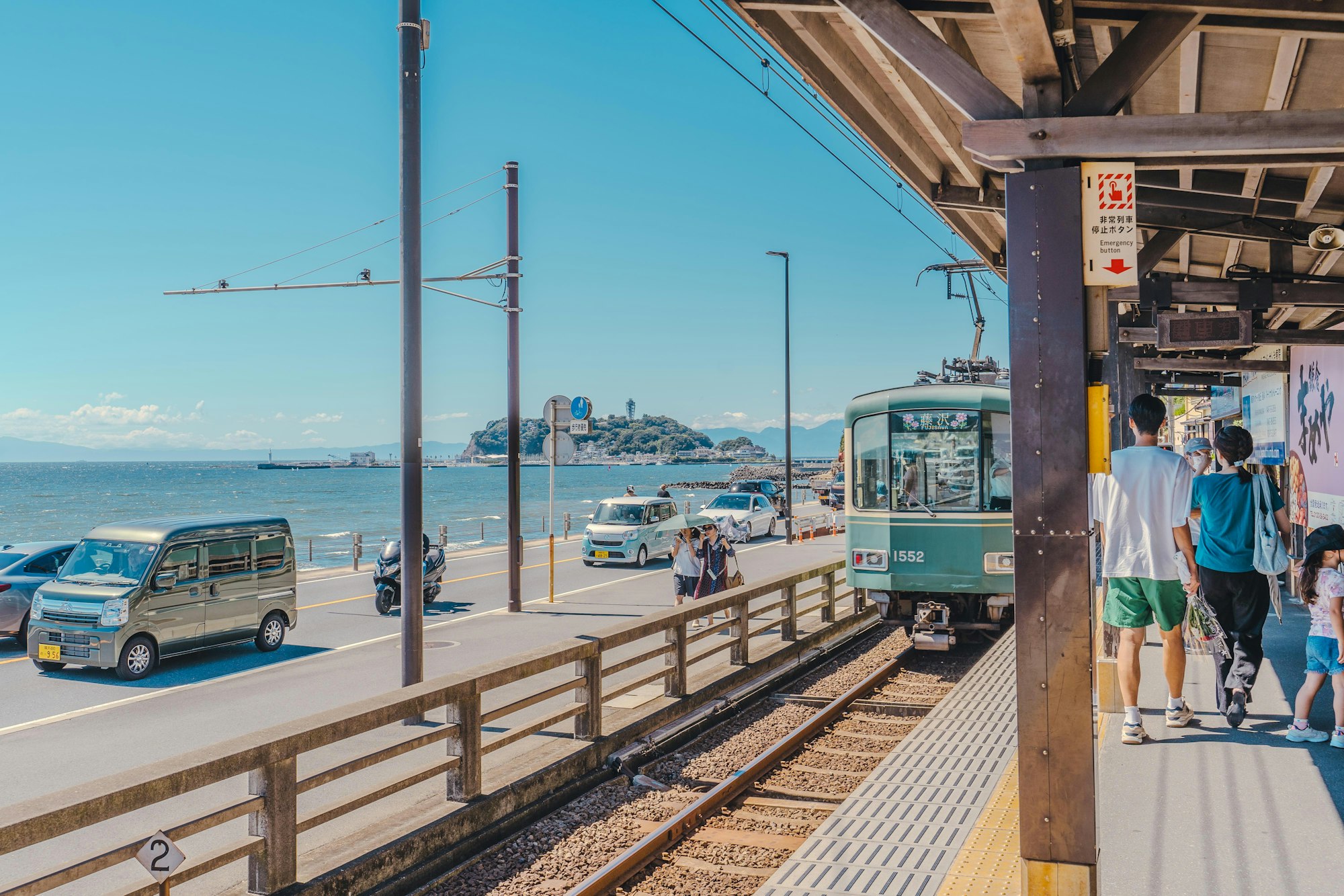 Enoden train at a seaside station on the Kamakura coast with Enoshima island in the distance