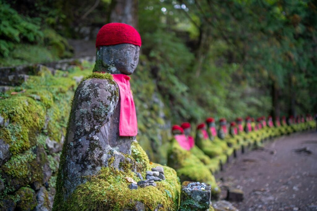 Moss-covered jizo statues with red caps along the path at Kanmangafuchi Abyss