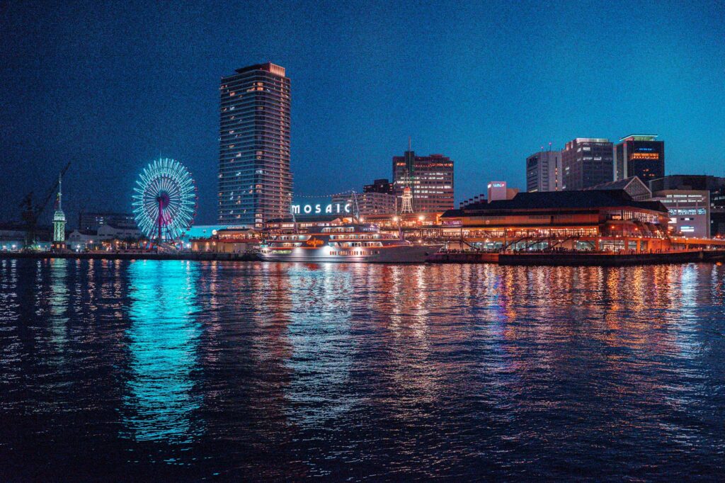 The lit-up Ferris wheel and hotels of Kobe Harborland reflected in the harbor at night
