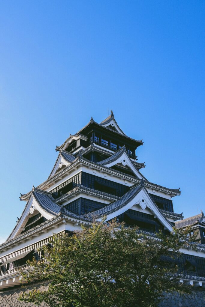 The black-and-white main keep of Kumamoto Castle under a blue sky
