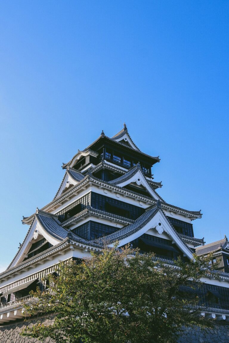 The black-and-white main keep of Kumamoto Castle under a blue sky