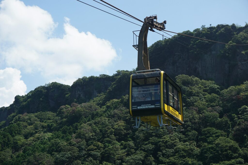 A yellow gondola of the Mount Nokogiri Ropeway climbing the forested mountainside