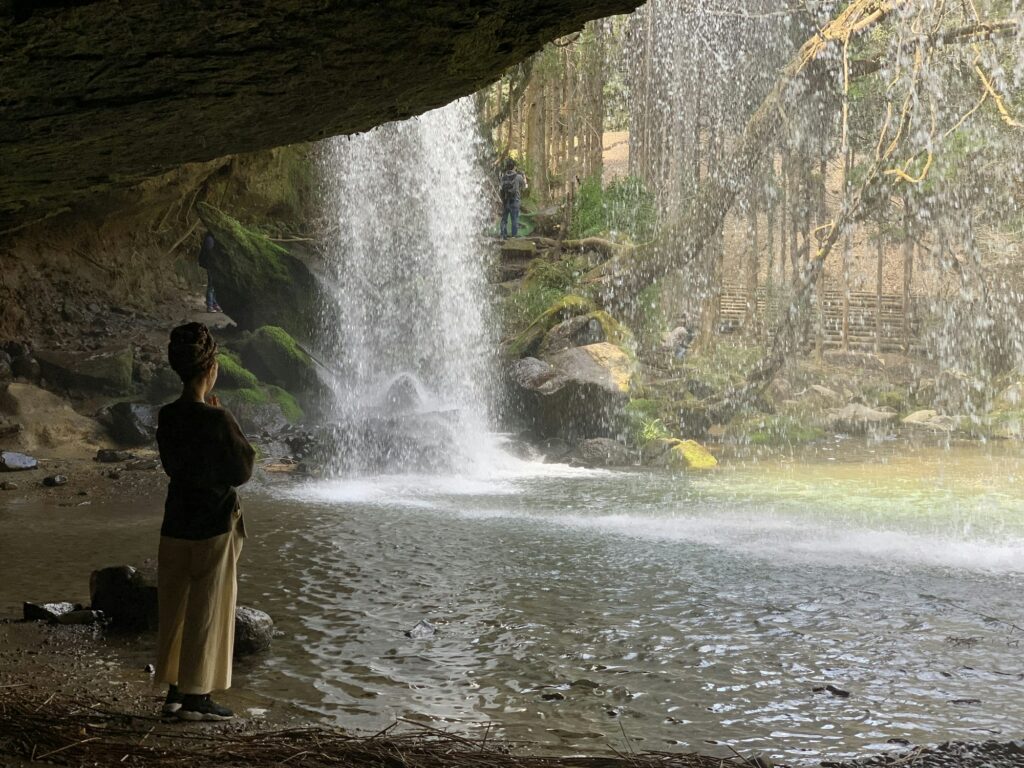 A visitor standing in the hollow behind the curtain of Nabegataki Falls in Oguni