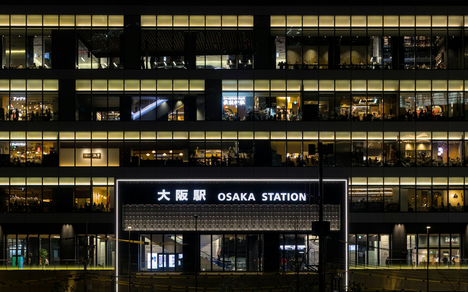 Osaka Station sign in English and Japanese in front of the lit-up station building at night