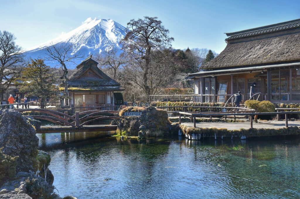Thatched buildings and a clear spring-fed pond at Oshino Hakkai village with Mount Fuji behind