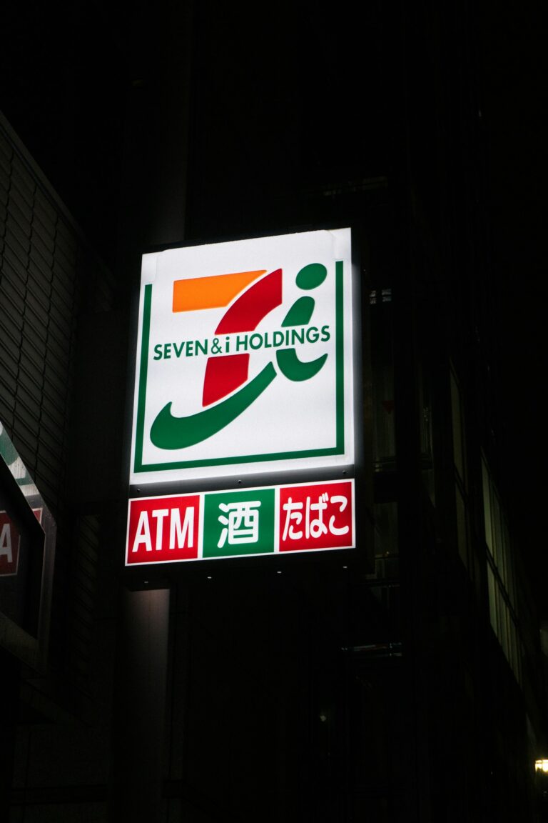Illuminated 7-Eleven sign with ATM and alcohol and tobacco panels at night in Japan