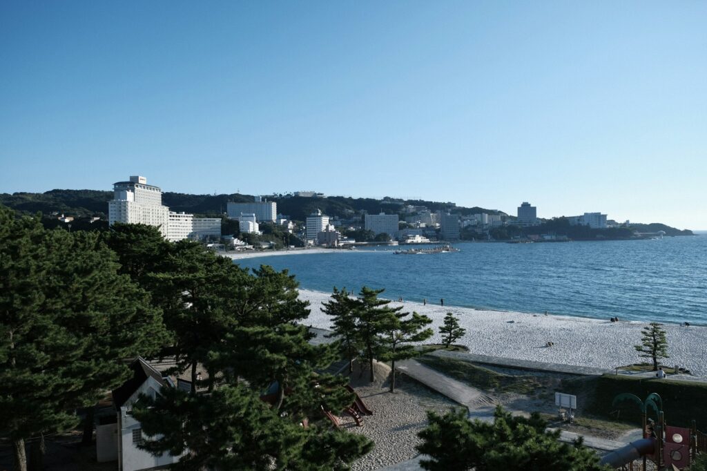 Hotels lining the white beach of Shirahama Onsen seen through pine trees