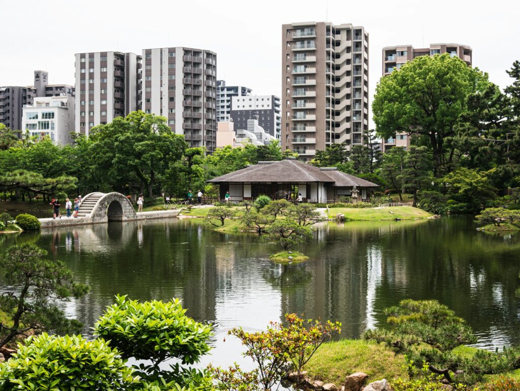 Pond, arched stone bridge and teahouse at Shukkeien Garden with the Hiroshima skyline behind