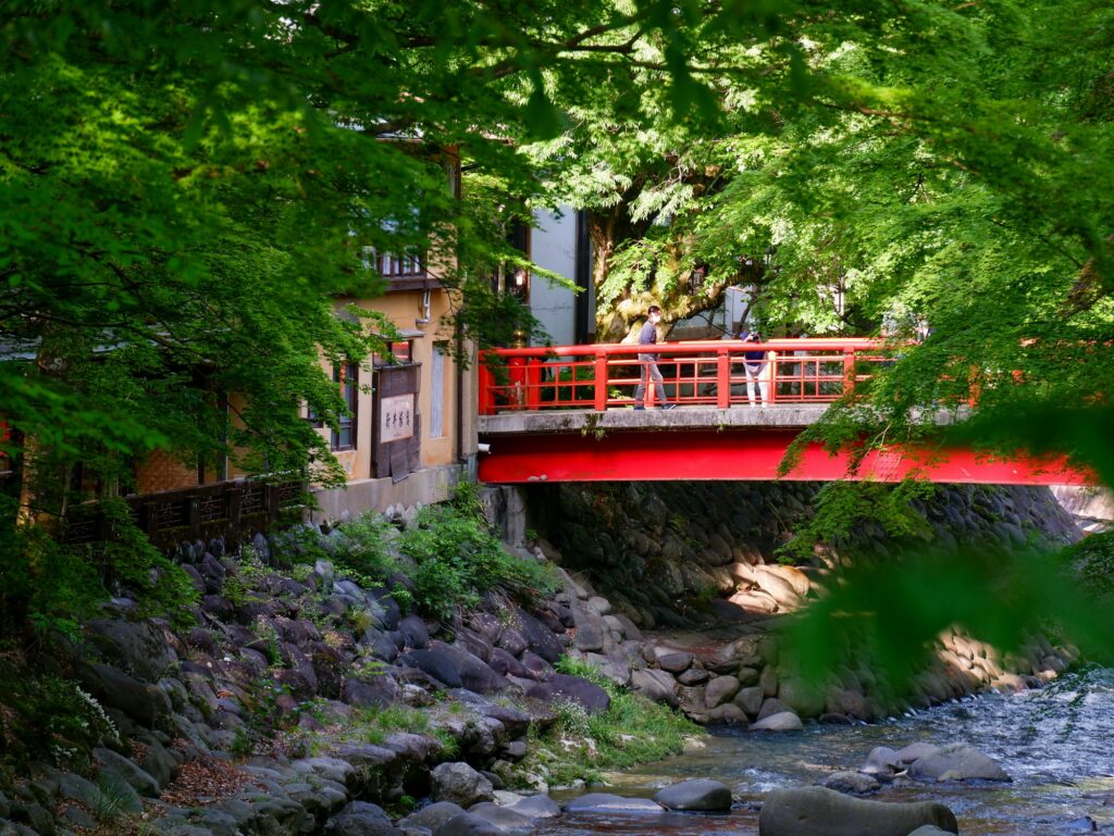 A red footbridge over the Katsura River among green trees in Shuzenji Onsen