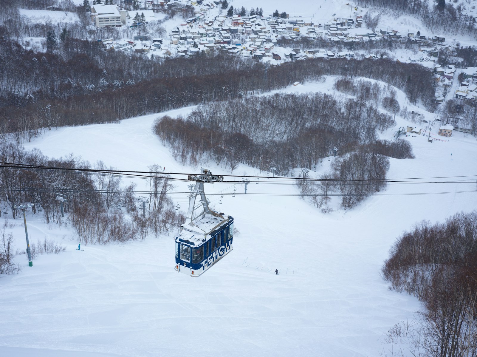 A gondola running above snowy ski slopes and forest in Japan