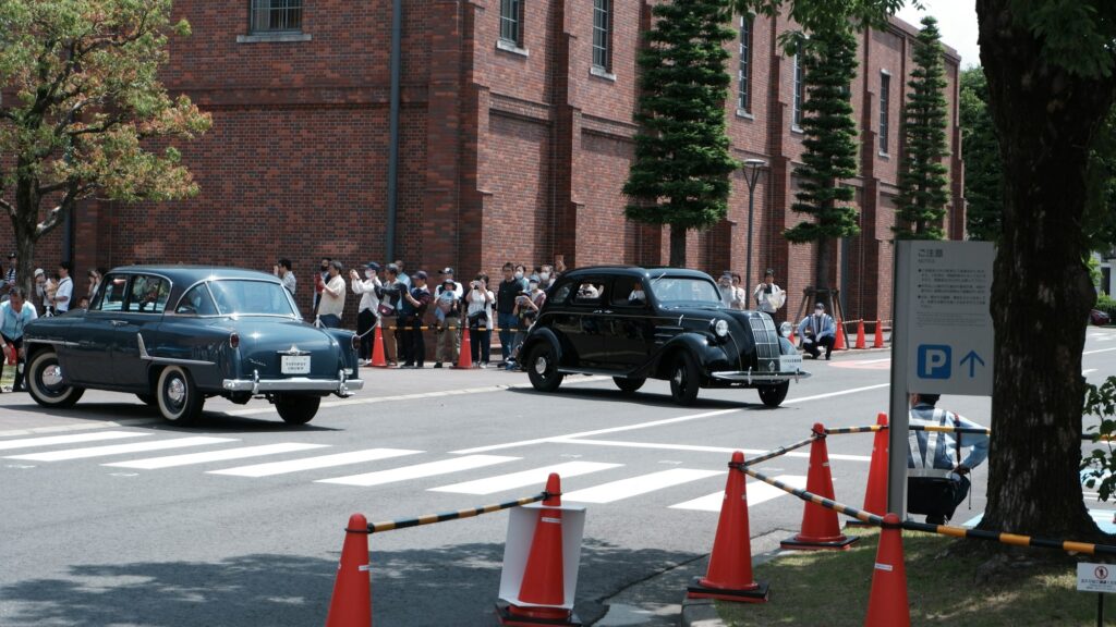 Vintage cars driving past the red-brick building of the Toyota Commemorative Museum of Industry and Technology