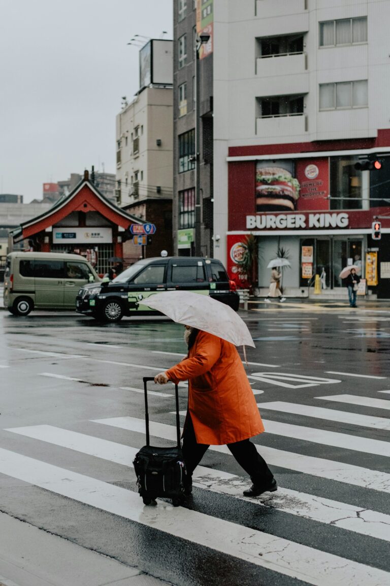 A traveler pulls a suitcase across a rainy Tokyo crosswalk.