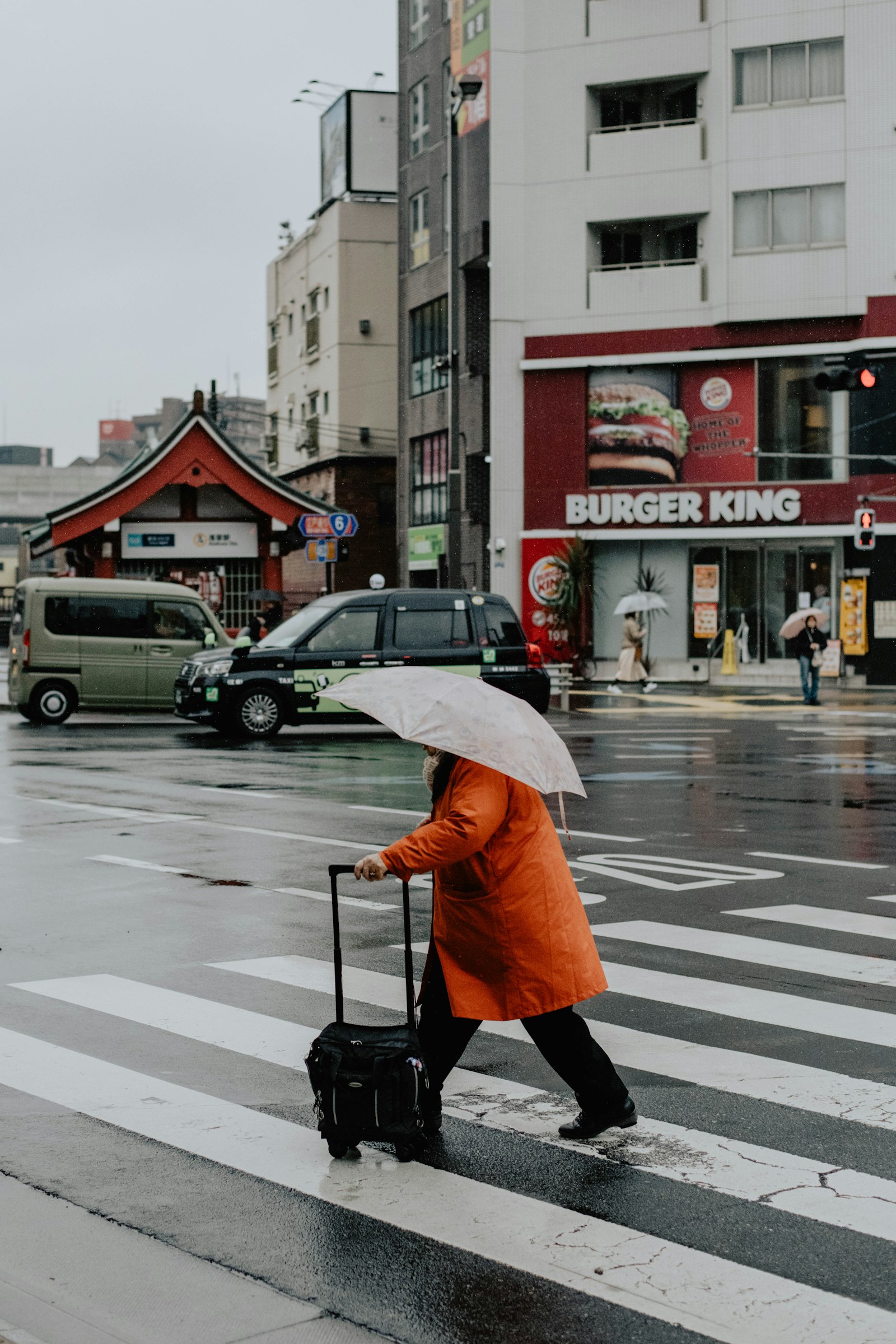 A traveler pulls a suitcase across a rainy Tokyo crosswalk.