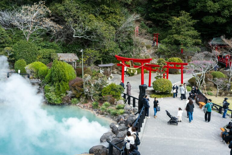 Steam rising over the blue pond of Umi Jigoku with a red torii in Beppu