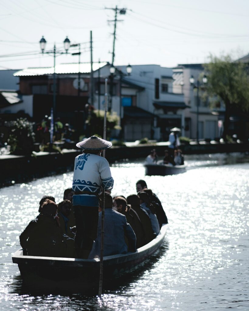 A boatman in a straw hat poling a punt full of passengers along a canal in Yanagawa